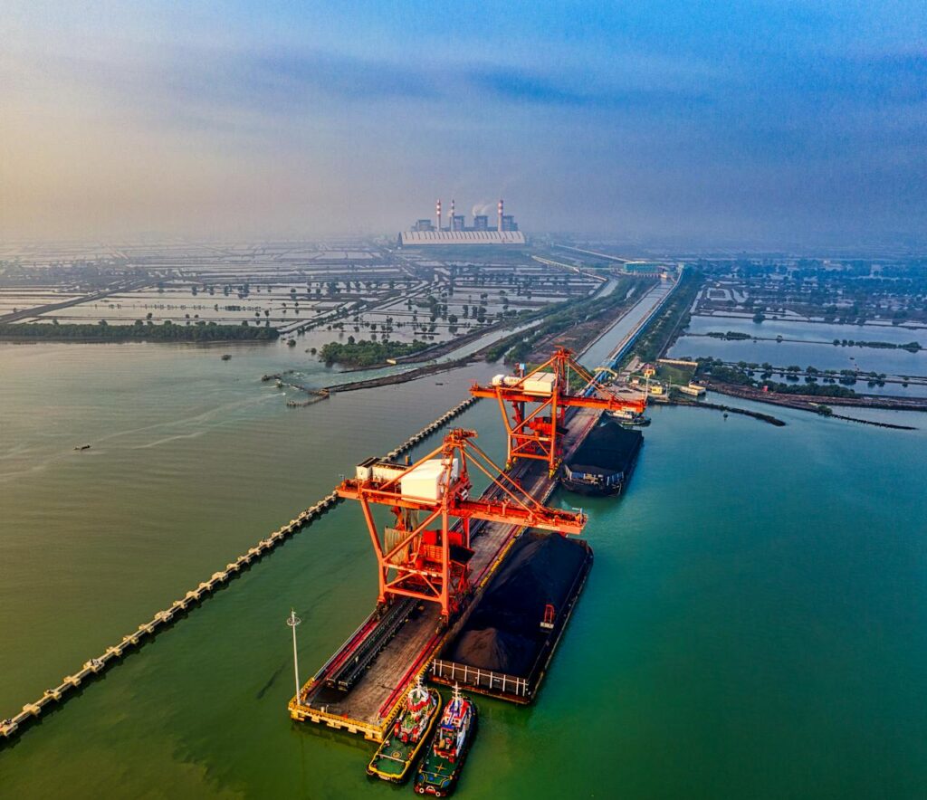 Stunning aerial view of a bustling industrial port in Banten, Indonesia with cranes and cargo ships.